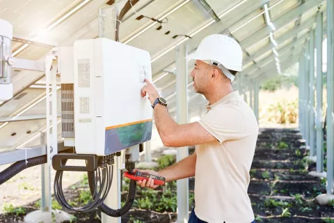 Ein Elektriker installiert einen Wechselrichter unterhalb einer Solar-Anlage.